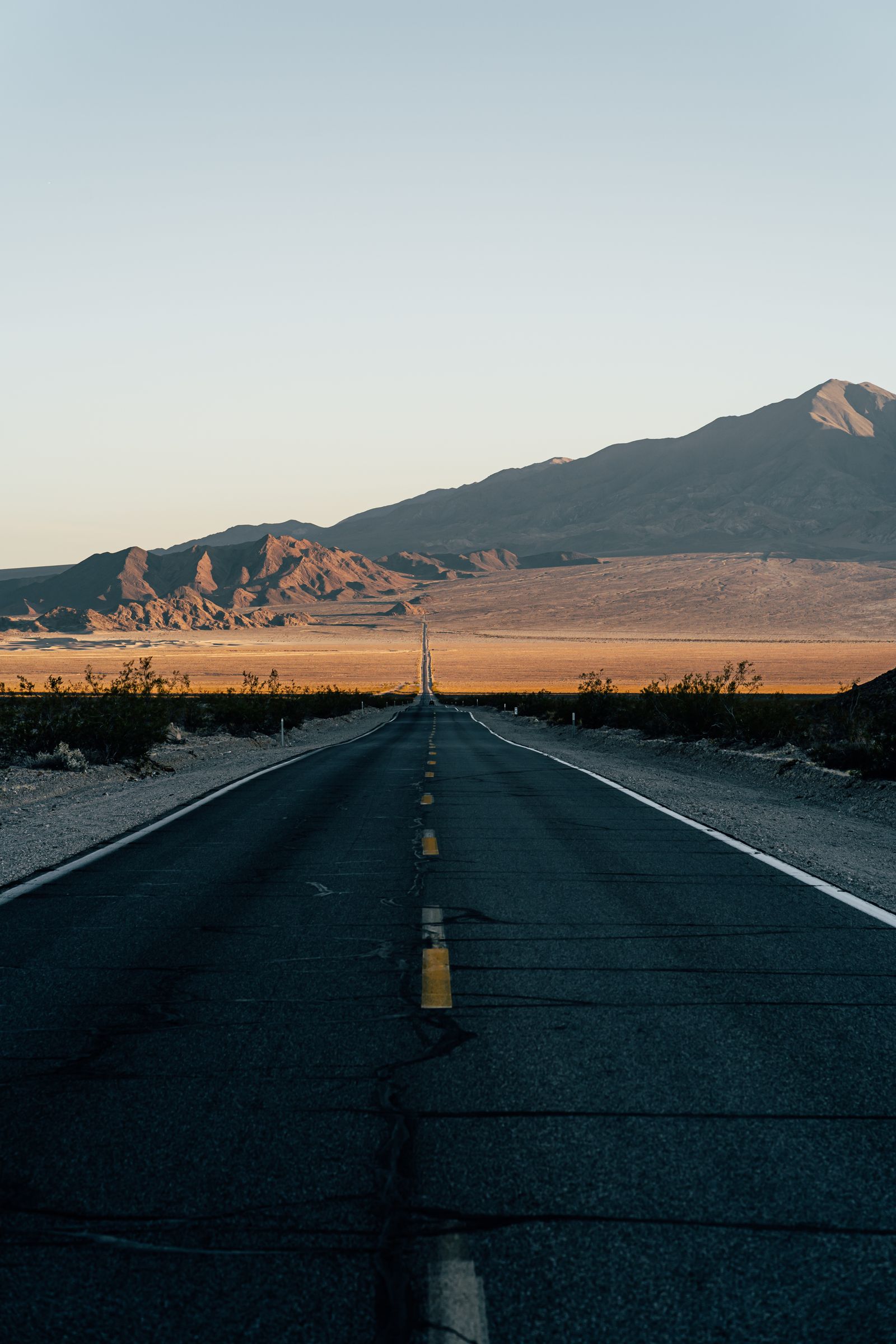 An empty two-lane road running straight toward desert mountains in early morning light.