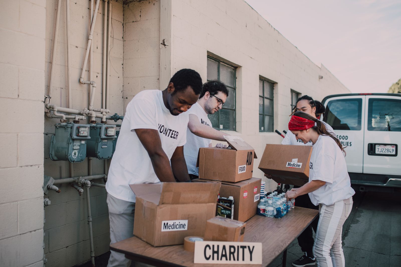 Four volunteers in printed T-shirts sorting cardboard boxes marked food and medicine on a trestle table.